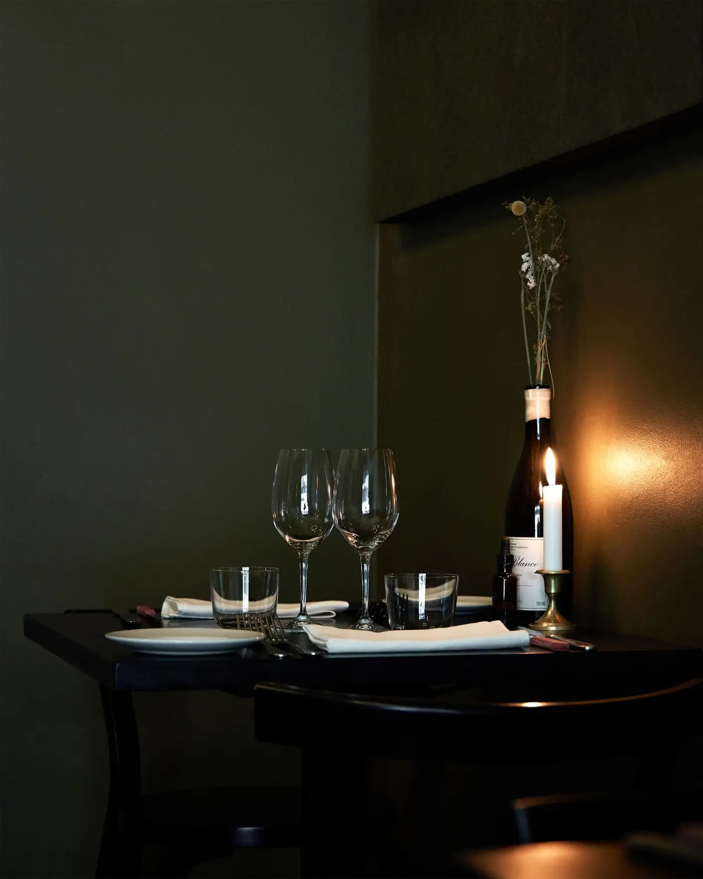 A corner table set for two with wine glasses and a lit candle