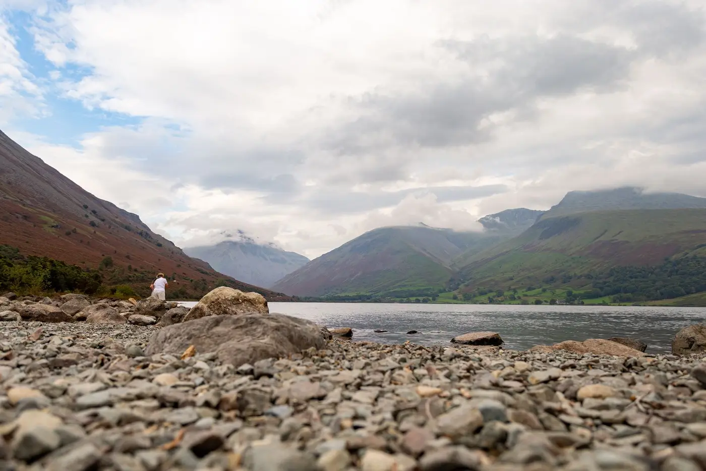 A still lake beneath high fells under a bright, cloudy sky